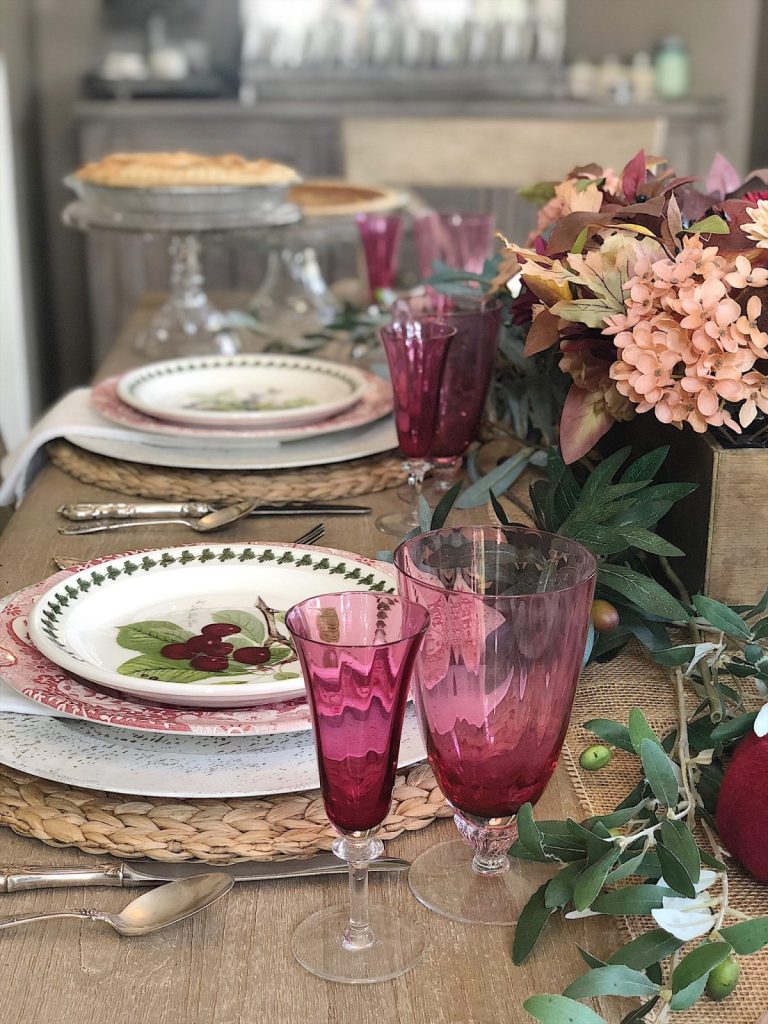 A table set for breakfast with cranberry glasses and plates, and a centerpiece. It's set to enjoy pice for breakfast on the day after Thanksgiving.