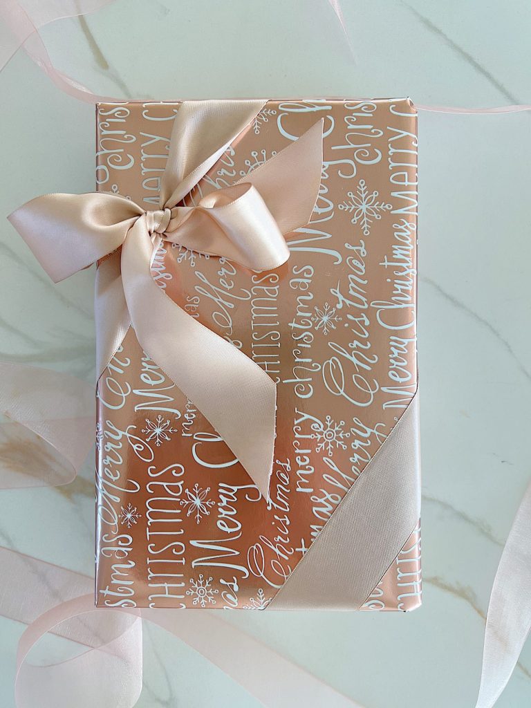 Instructions to tie a bow with ribbon on your Christmas gifts using rose gold metallic wrapping paper and assorted ribbons.
