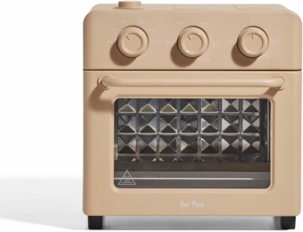 This beige countertop oven, with three control knobs and a transparent door, features a diamond-patterned interior that adds a touch of elegance, much like the charm of a flocked Christmas tree.