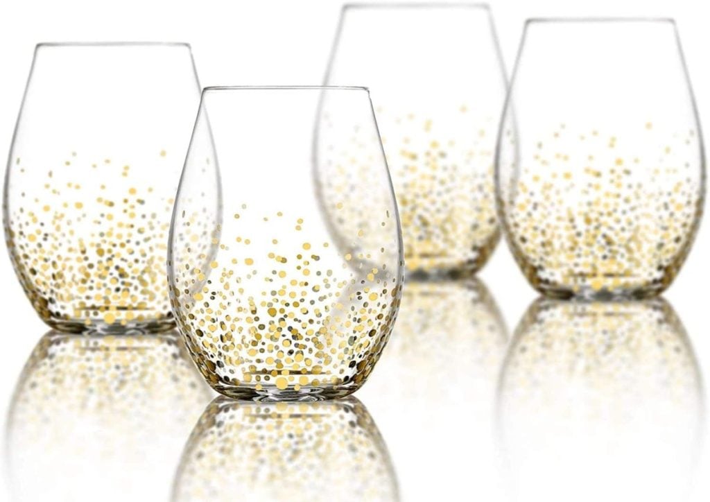 Four stemless wine glasses with gold and silver dotted designs are arranged on a reflective surface, perfect to set a festive Christmas table.