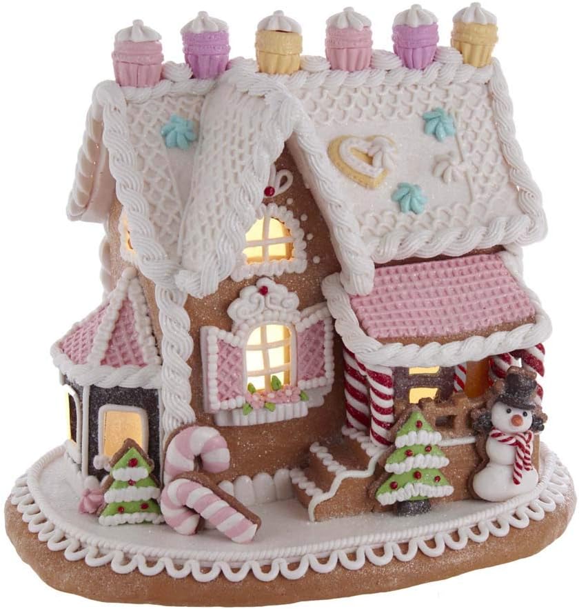 A Christmas gingerbread house with frosting decorations, candy canes, and a snowman. Cupcakes adorn the roof, and windows glow with light.