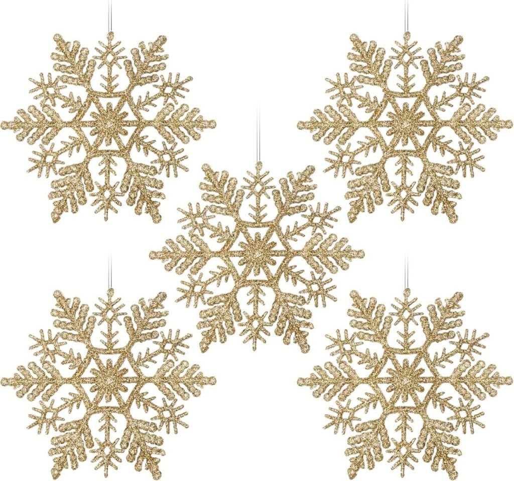 Five gold glitter snowflake ornaments hang elegantly against a white background, ready to add sparkle and charm as you set a Christmas table.