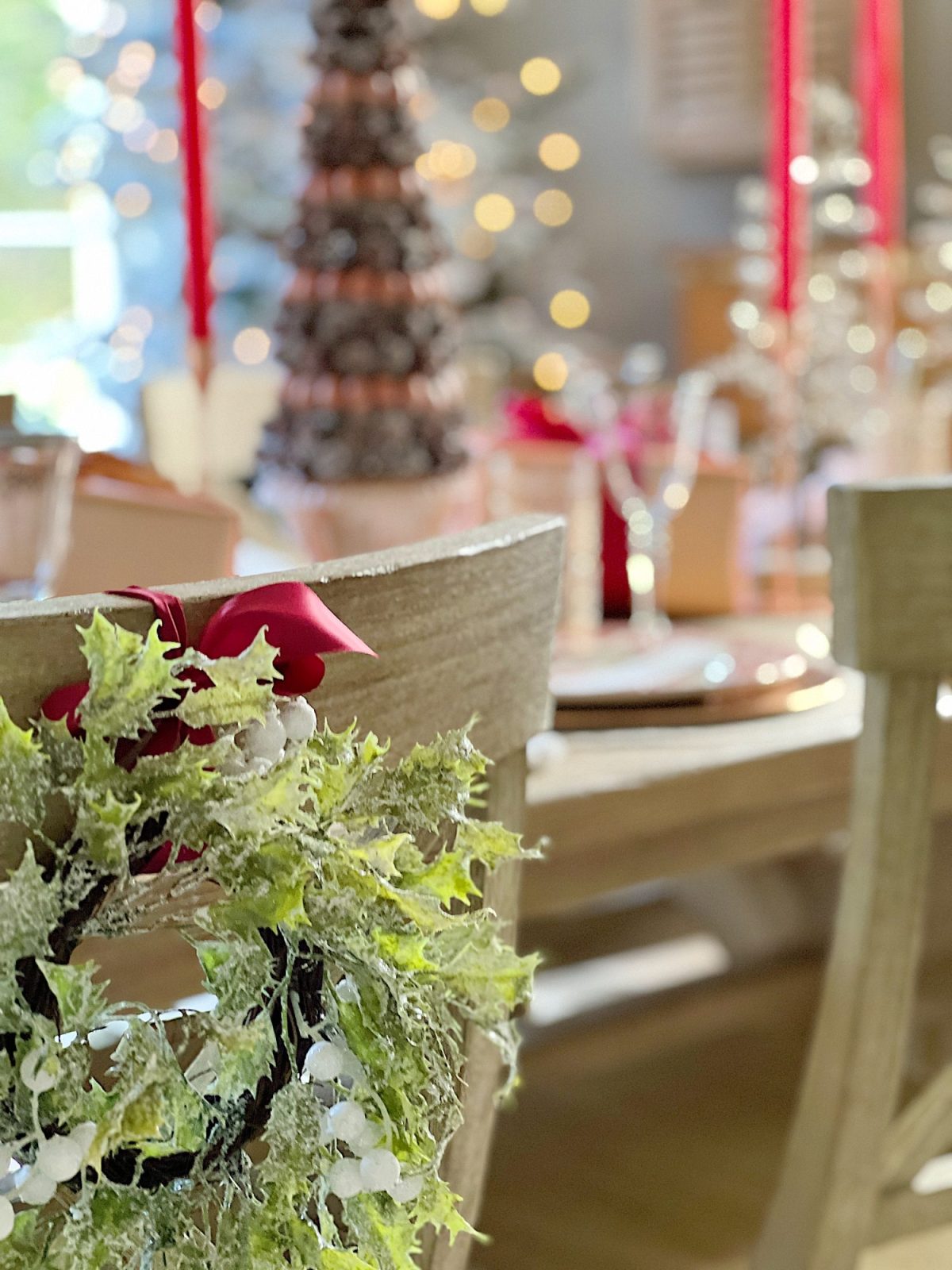 A Christmas table set in cranberry and rose gold colors with a DIY tree, cranberry and white plates, amber and clear glasses, rose gold chargers, and wrapped packages.