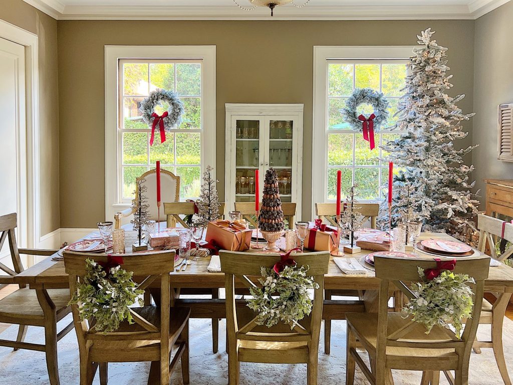 A Christmas table set in cranberry and rose gold colors with a DIY tree, cranberry and white plates, amber and clear glasses, rose gold chargers, and wrapped packages.