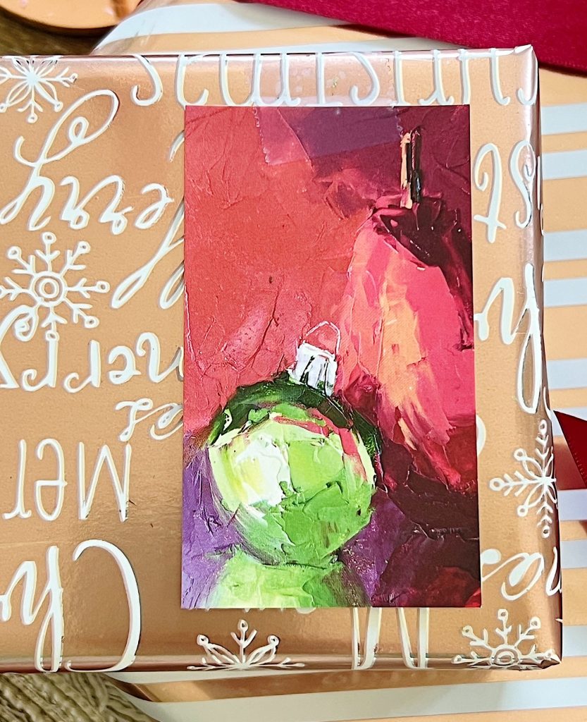 A Christmas table set in cranberry and rose gold colors with a DIY tree, cranberry and white plates, amber and clear glasses, rose gold chargers, and wrapped packages.