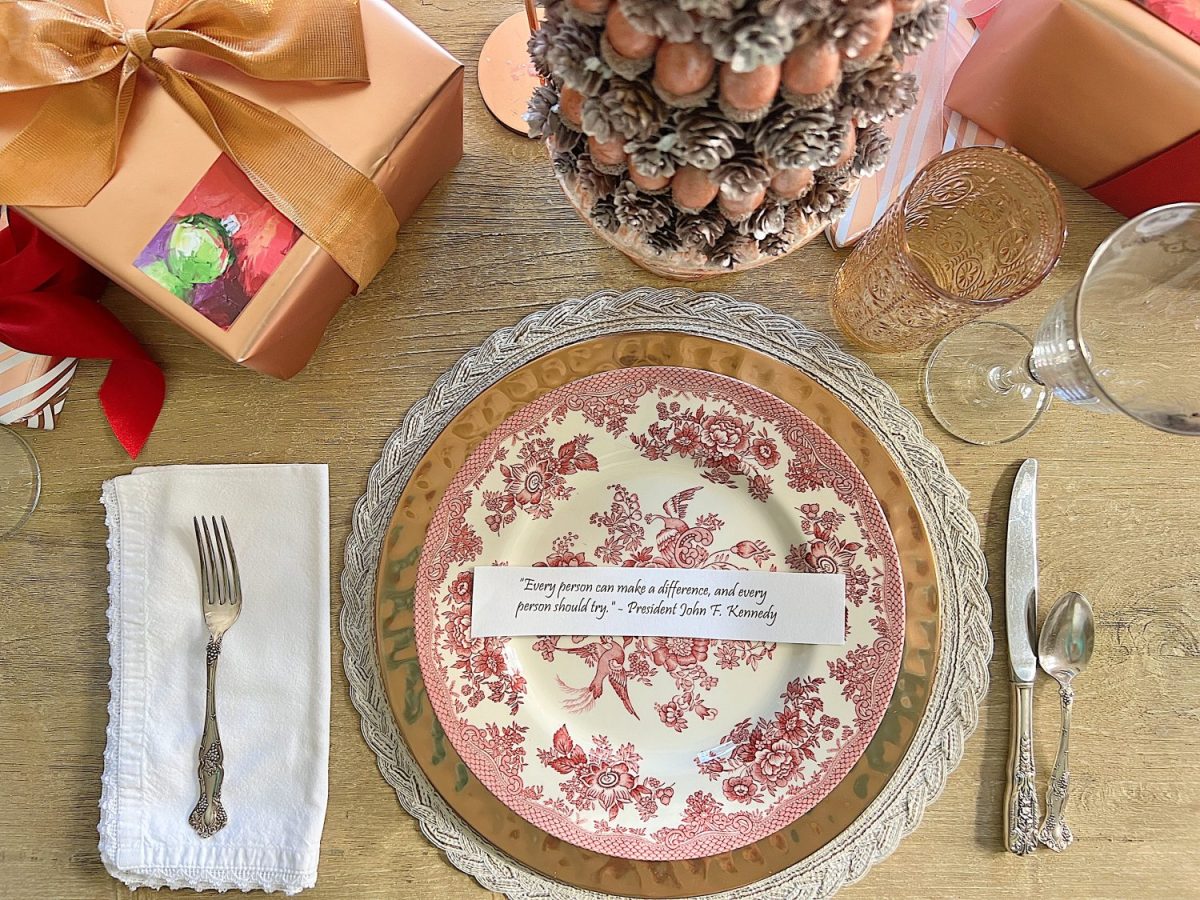 A Christmas table set in cranberry and rose gold colors with a DIY tree, cranberry and white plates, amber and clear glasses, rose gold chargers, and wrapped packages.