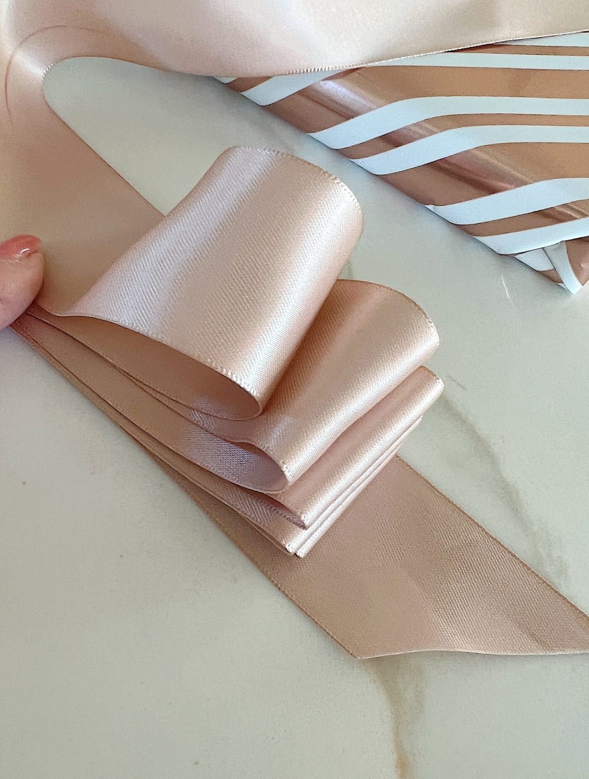 Instructions to tie a bow with ribbon on your Christmas gifts using rose gold metallic wrapping paper and assorted ribbons.