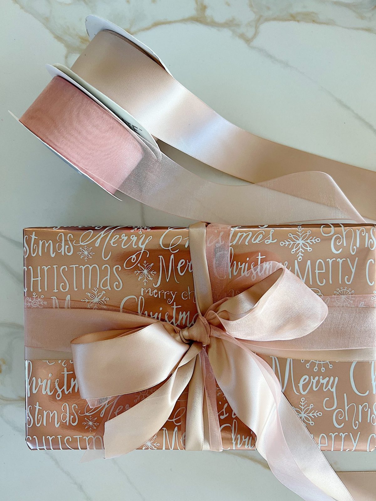 Instructions to tie a bow with ribbon on your Christmas gifts using rose gold metallic wrapping paper and assorted ribbons.