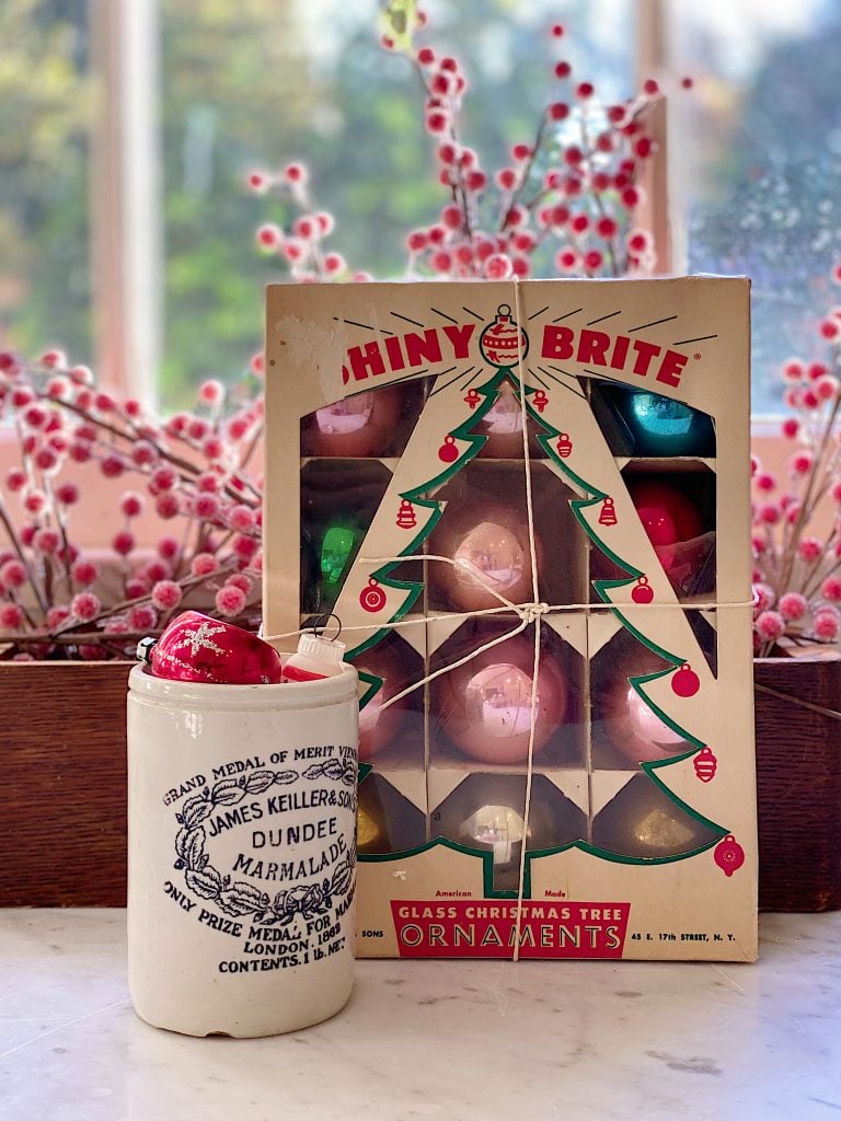 A box of Shiny Brite vintage ornaments and an english jar with red berries.
