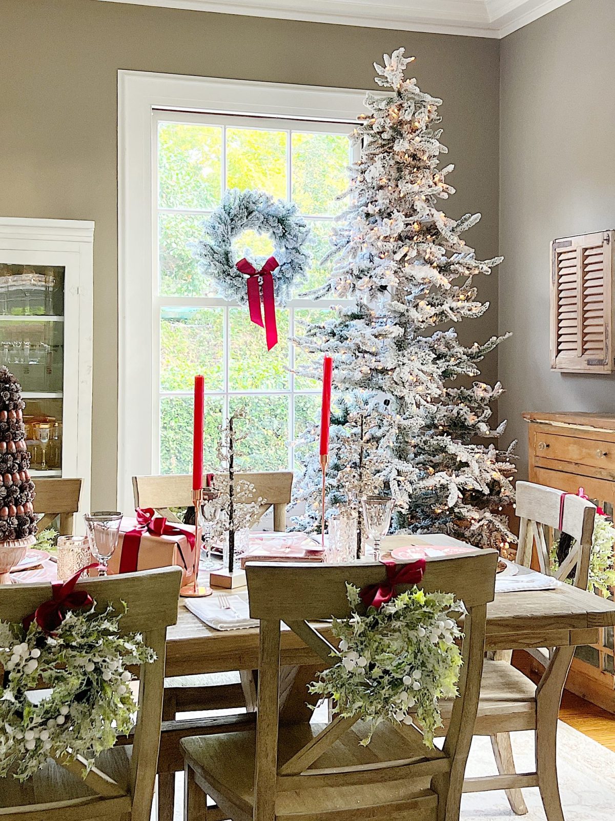 A Christmas table set in cranberry and rose gold colors with a DIY tree, cranberry and white plates, amber and clear glasses, rose gold chargers, and wrapped packages.