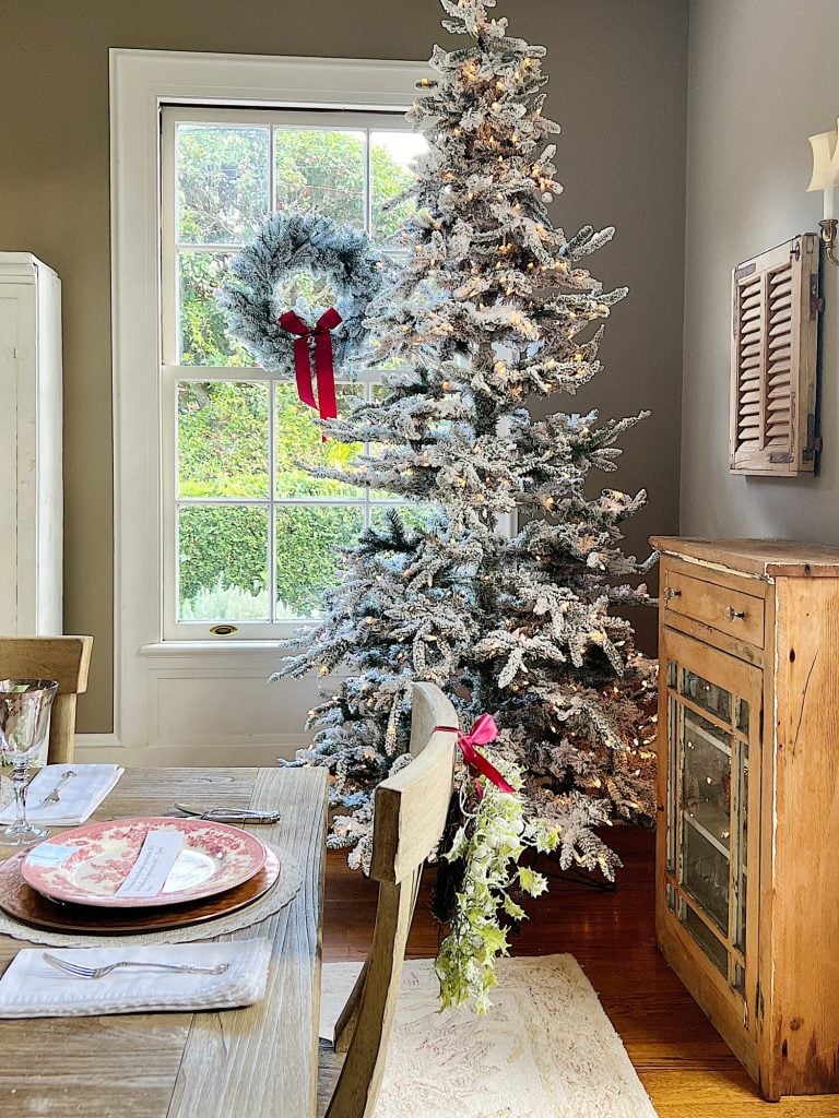 A Christmas table set in cranberry and rose gold colors with a DIY tree, cranberry and white plates, amber and clear glasses, rose gold chargers, and wrapped packages.