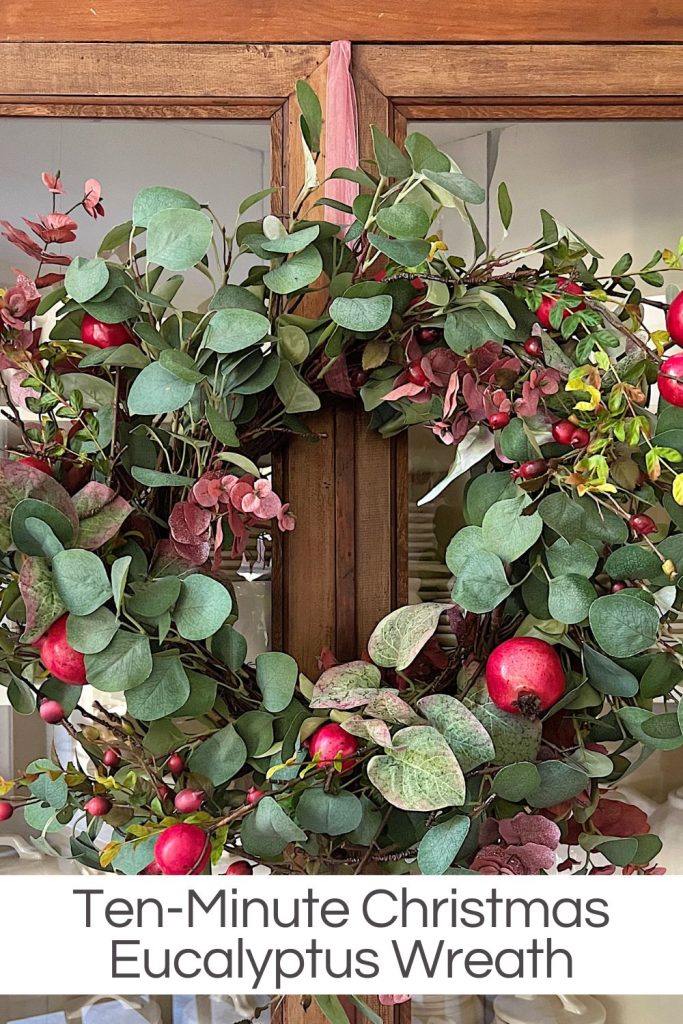 A eucalyptus wreath made in ten minutes with faux flowers and pomegranates hanging on a window.