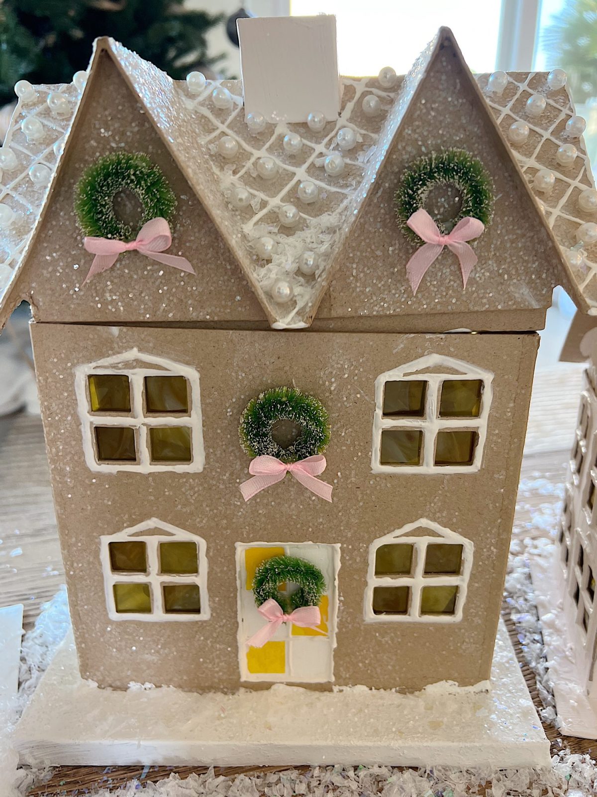 Gingerbread houses made from cardboard and decorated with paint, puff pens, pearls, glitter, tiny wreaths, and pink bows, in a color palette of pink and white.