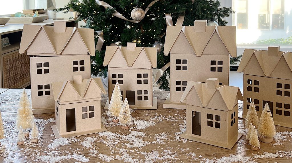 Gingerbread houses made from cardboard and decorated with paint, puff pens, pearls, glitter, tiny wreaths, and pink bows, in a color palette of pink and white.
