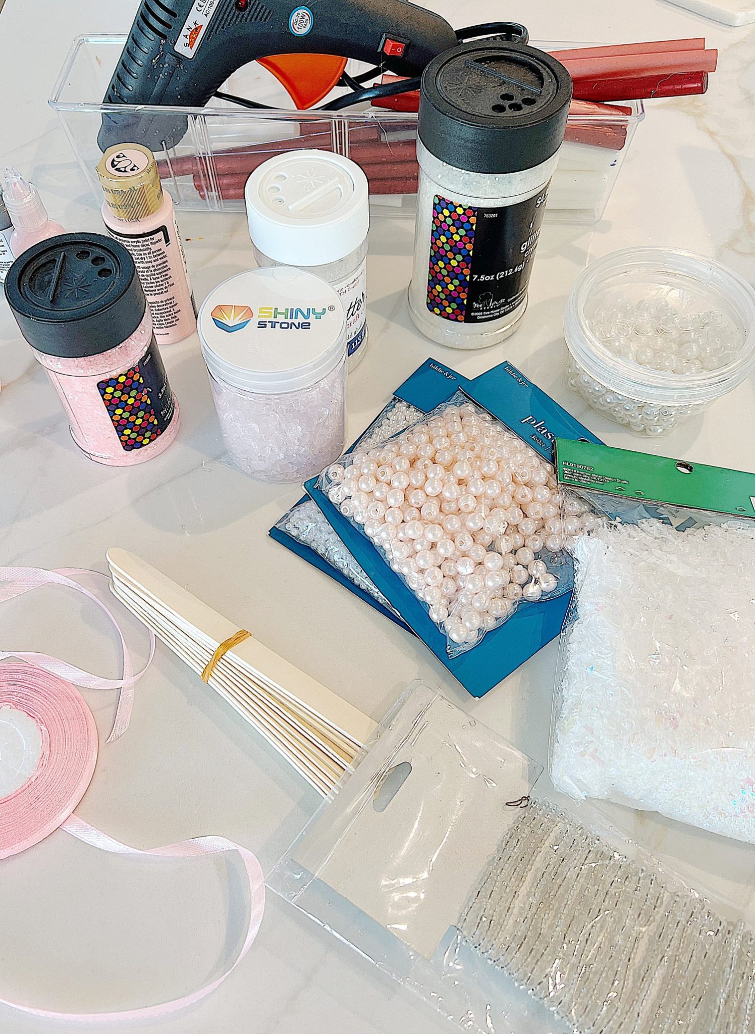 Gingerbread houses made from cardboard and decorated with paint, puff pens, pearls, glitter, tiny wreaths, and pink bows, in a color palette of pink and white.