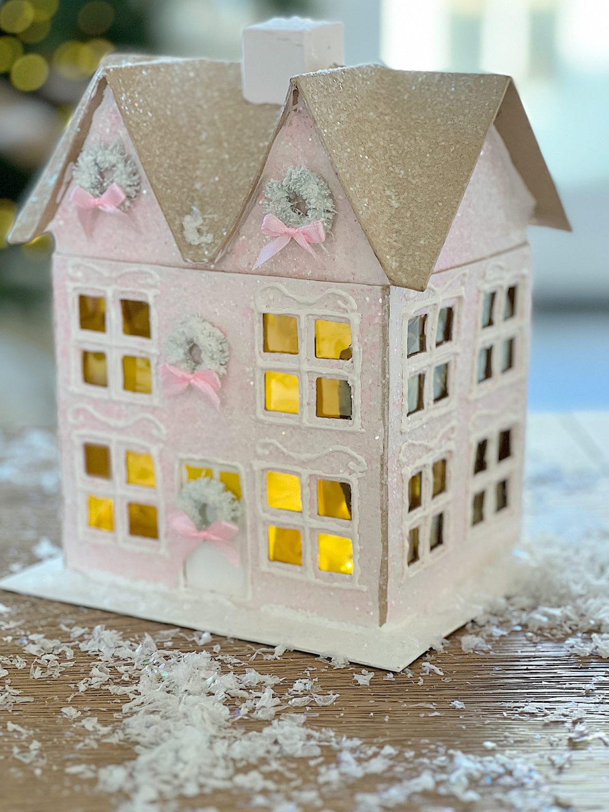 Gingerbread houses made from cardboard and decorated with paint, puff pens, pearls, glitter, tiny wreaths, and pink bows, in a color palette of pink and white.