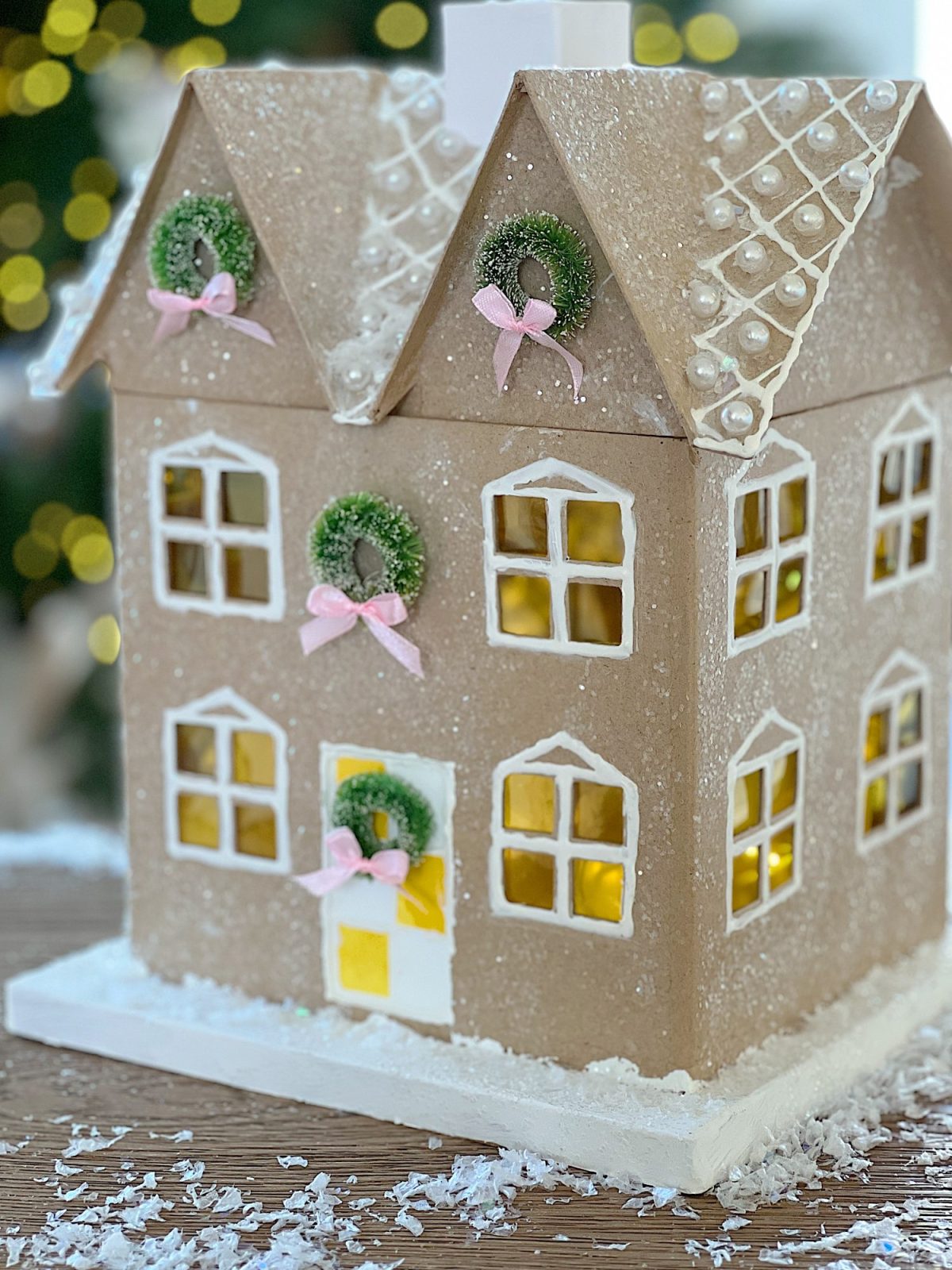 Gingerbread houses made from cardboard and decorated with paint, puff pens, pearls, glitter, tiny wreaths, and pink bows, in a color palette of pink and white.