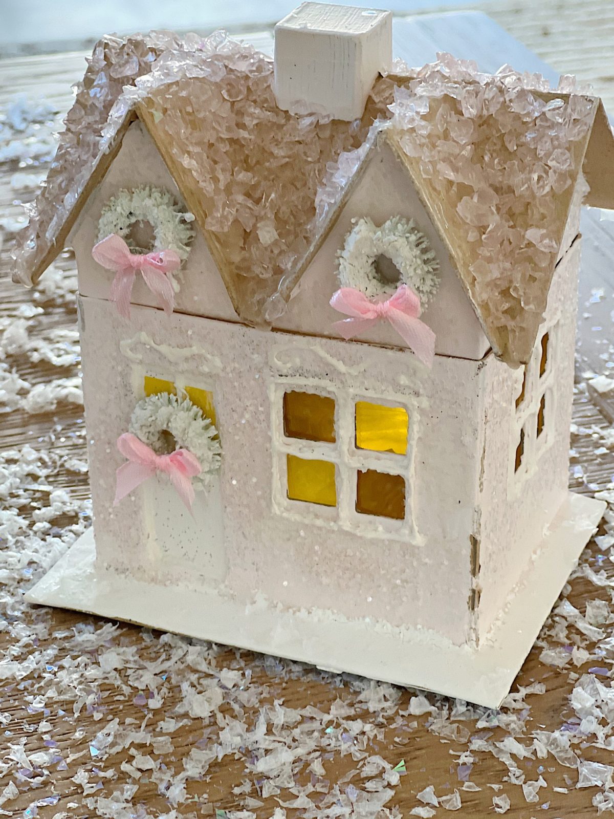 Gingerbread houses made from cardboard and decorated with paint, puff pens, pearls, glitter, tiny wreaths, and pink bows, in a color palette of pink and white.