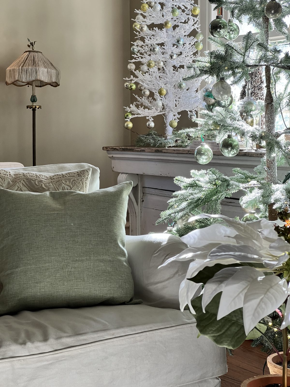 A living room decorated in neutral colors of tan, white, silver, and light green with silver frosted trees, white poinsettias and more holiday decor.