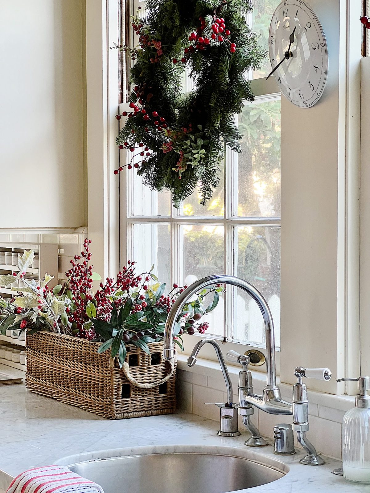 Our white kitchen decorated with wreaths in the windows and on the back of the counter stools, red, green, and white trees, red and white towels, and more.