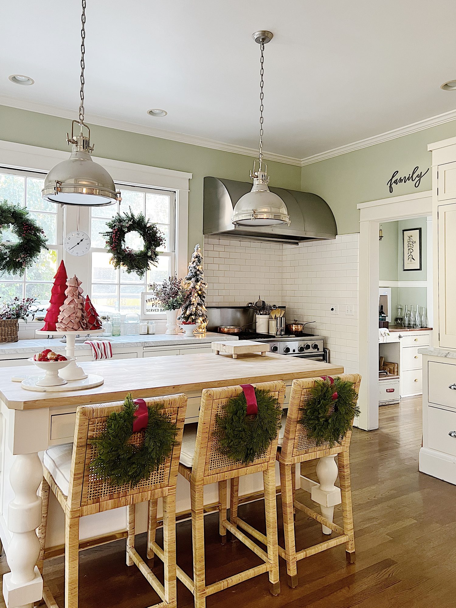 Our white kitchen decorated with wreaths in the windows and on the back of the counter stools, red, green, and white trees, red and white towels, and more.