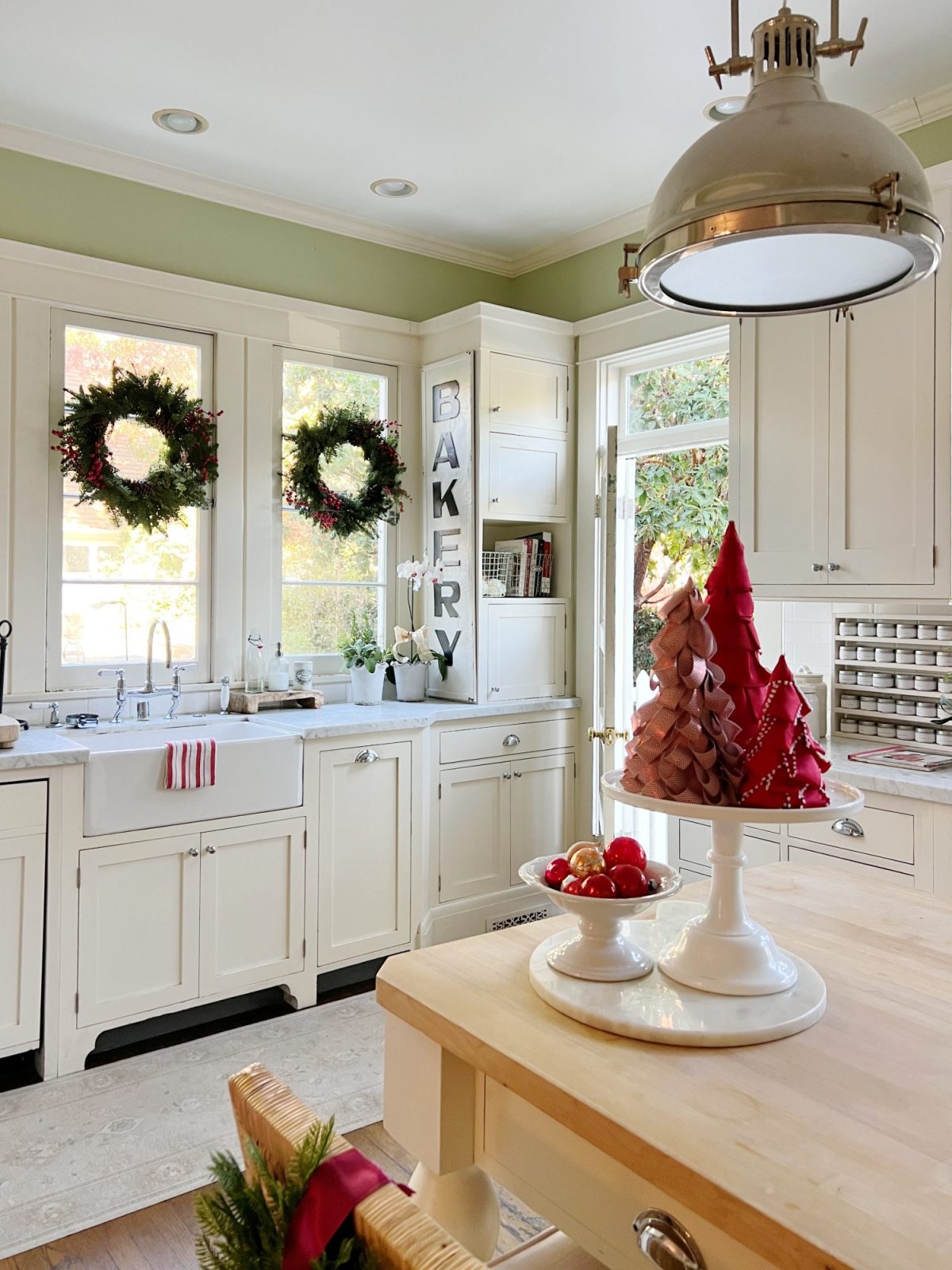 Our white kitchen decorated with wreaths in the windows and on the back of the counter stools, red, green, and white trees, red and white towels, and more.