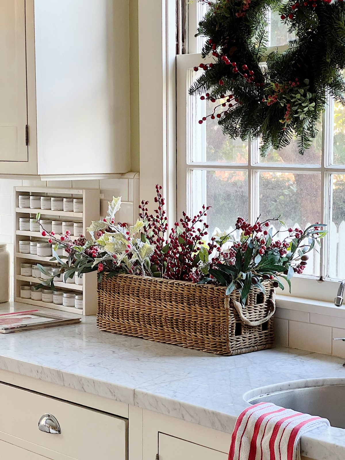 Our white kitchen decorated with wreaths in the windows and on the back of the counter stools, red, green, and white trees, red and white towels, and more.