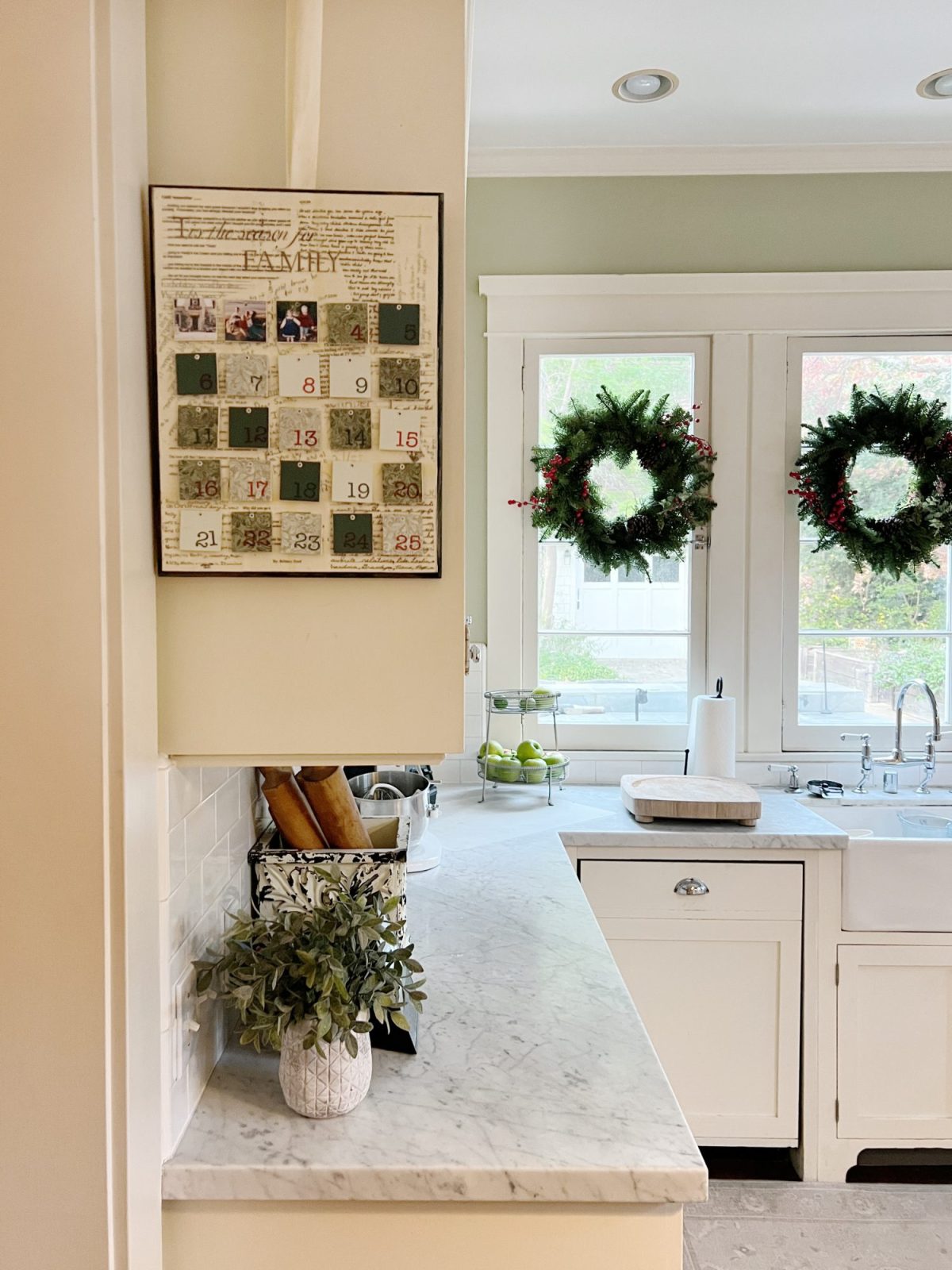 Our white kitchen decorated with wreaths in the windows and on the back of the counter stools, red, green, and white trees, red and white towels, and more.