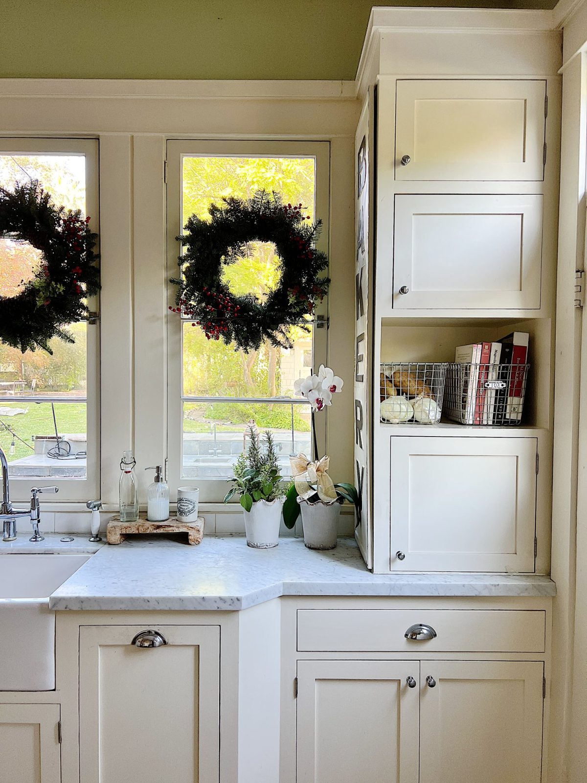Our white kitchen decorated with wreaths in the windows and on the back of the counter stools, red, green, and white trees, red and white towels, and more.