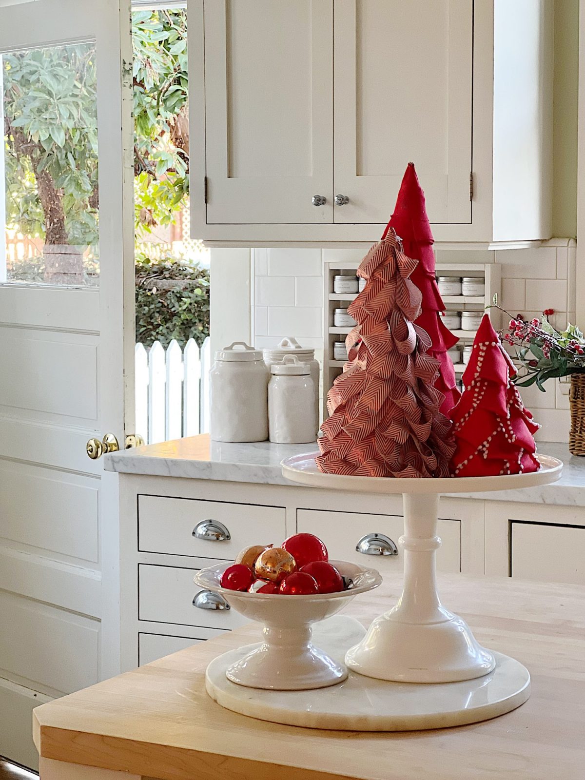 Our white kitchen decorated with wreaths in the windows and on the back of the counter stools, red, green, and white trees, red and white towels, and more.