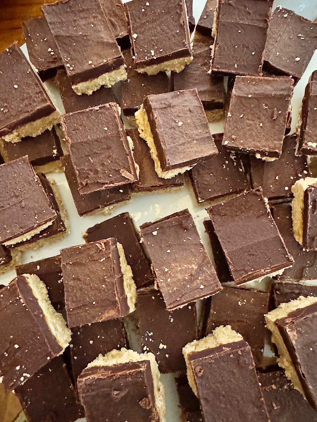 A pile of chocolate-covered layered squares with a creamy peanut butter fudge filling, arranged on a white surface.