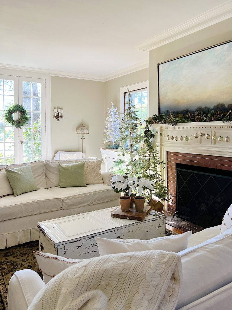 A living room decorated in neutral colors of tan, white, silver, and light green with silver frosted trees, white poinsettias and more holiday decor.