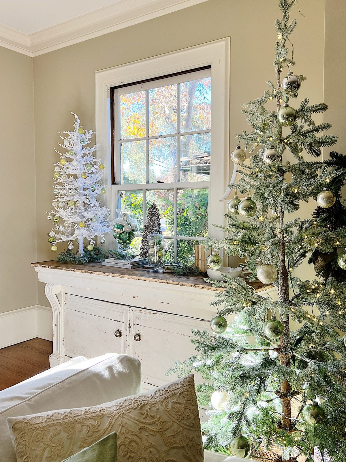 A living room decorated in neutral colors of tan, white, silver, and light green with silver frosted trees, white poinsettias and more holiday decor.