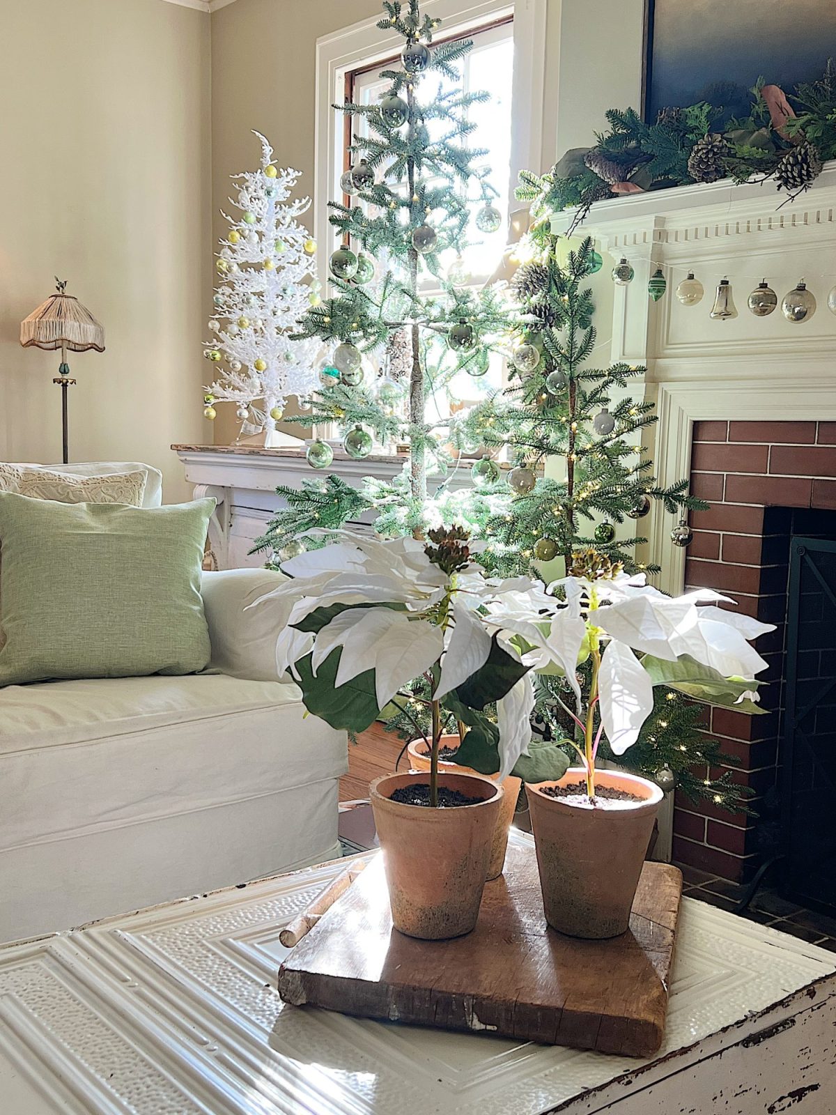 A living room decorated in neutral colors of tan, white, silver, and light green with silver frosted trees, white poinsettias and more holiday decor.