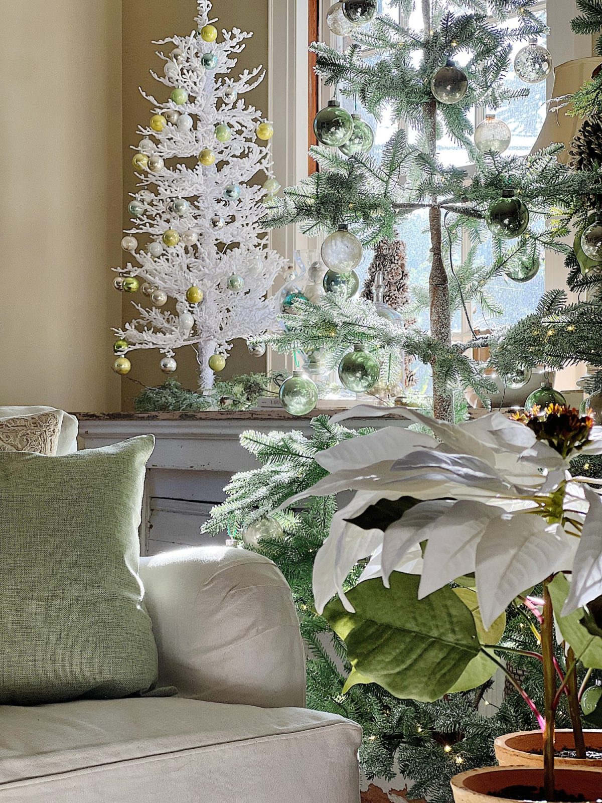 A living room decorated in neutral colors of tan, white, silver, and light green with silver frosted trees, white poinsettias and more holiday decor.