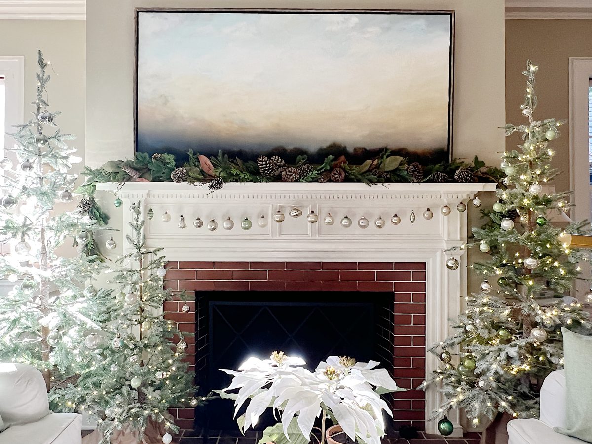 A living room decorated in neutral colors of tan, white, silver, and light green with silver frosted trees, white poinsettias and more holiday decor.