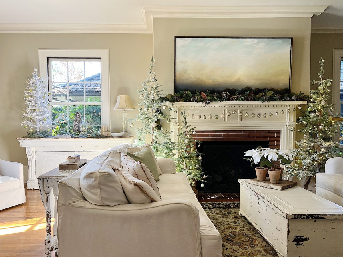 A living room decorated in neutral colors of tan, white, silver, and light green with silver frosted trees, white poinsettias and more holiday decor.