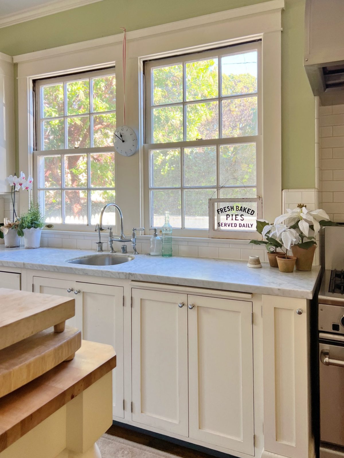 Our kitchen with new counter stools at the island, light green walls, white cabinets, and marble counter tops.