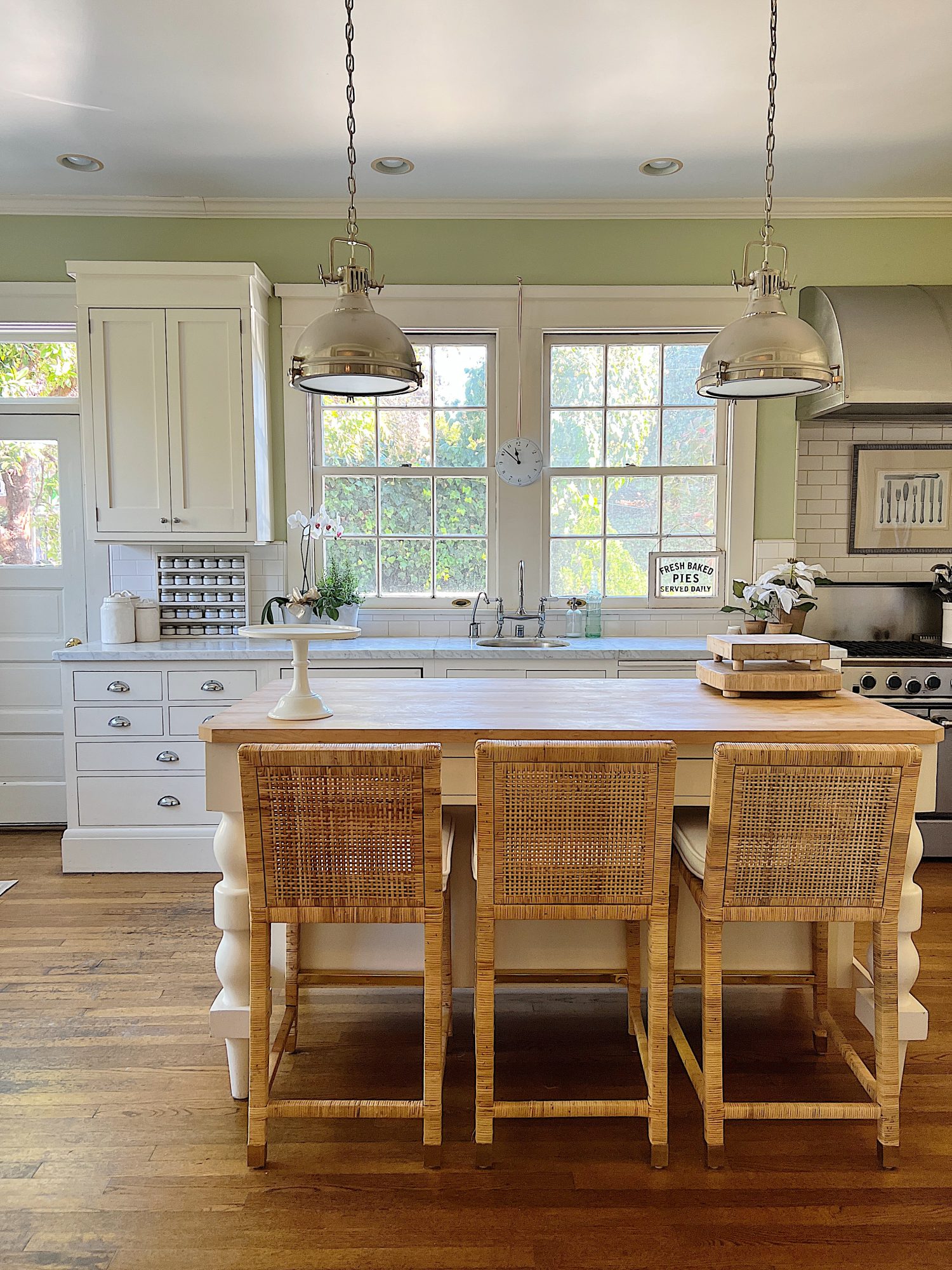 Our kitchen with new counter stools at the island, light green walls, white cabinets, and marble counter tops.