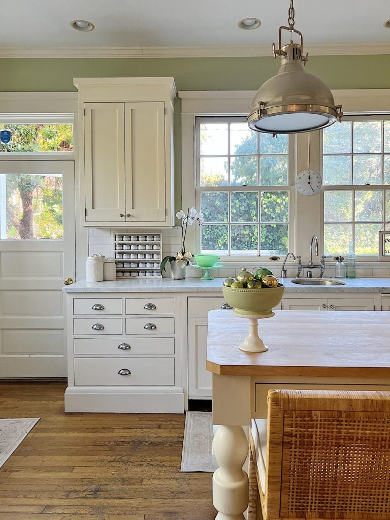 Our kitchen with new counter stools at the island, light green walls, white cabinets, and marble counter tops.