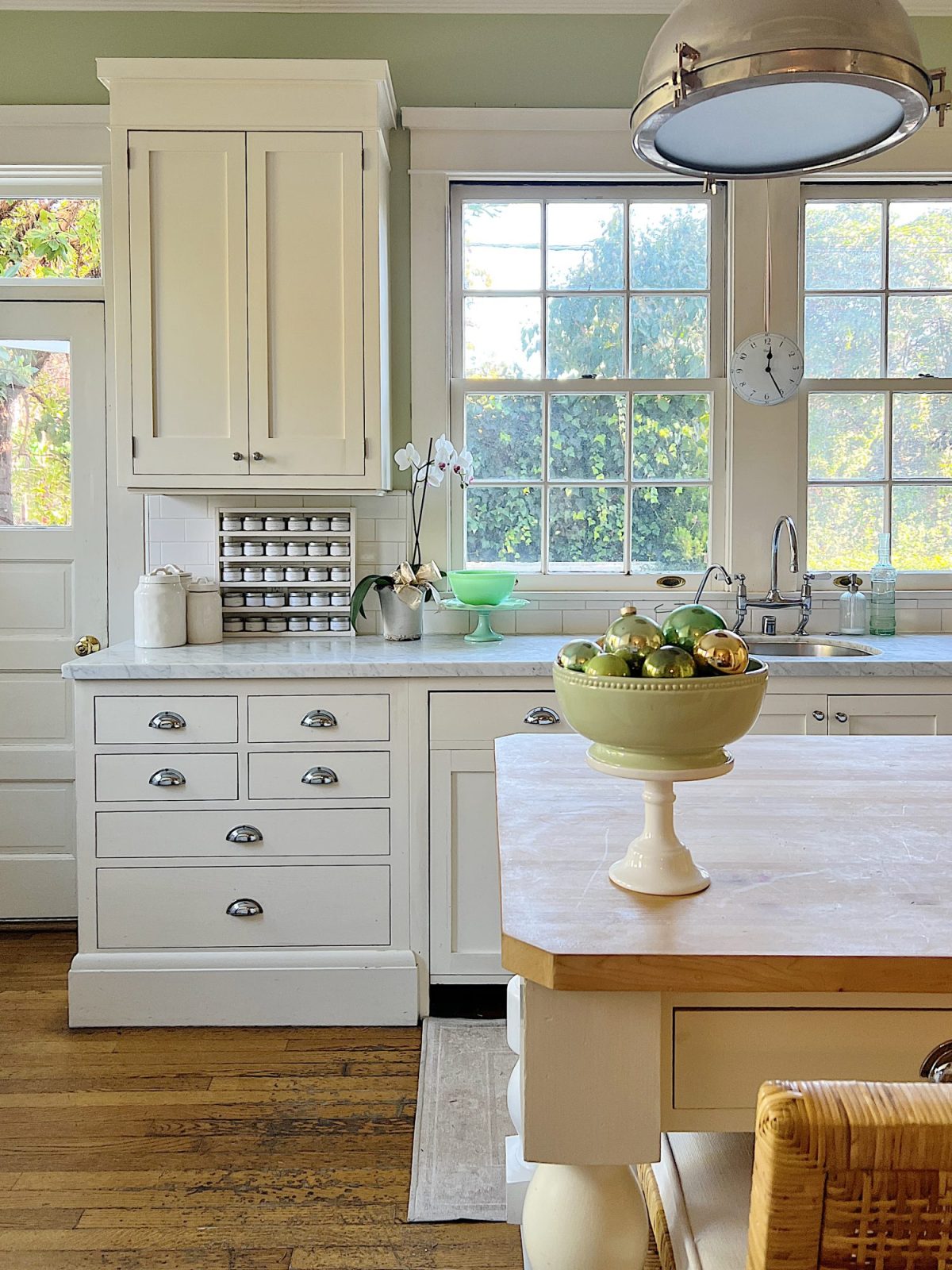 Our kitchen with new counter stools at the island, light green walls, white cabinets, and marble counter tops.