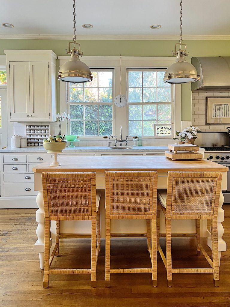 Our kitchen with new counter stools at the island, light green walls, white cabinets, and marble counter tops.