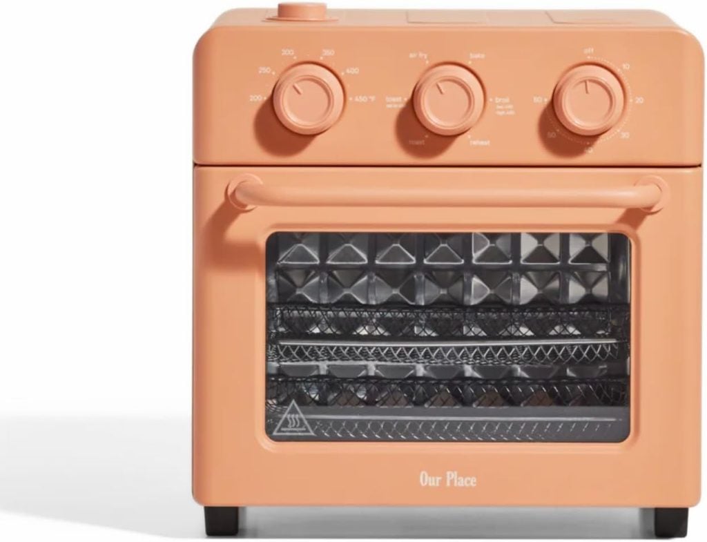 The orange countertop oven, featuring three control knobs and a clear front door, easily accommodates your culinary creations like baked parmesan crusted chicken on its three spacious wire racks.