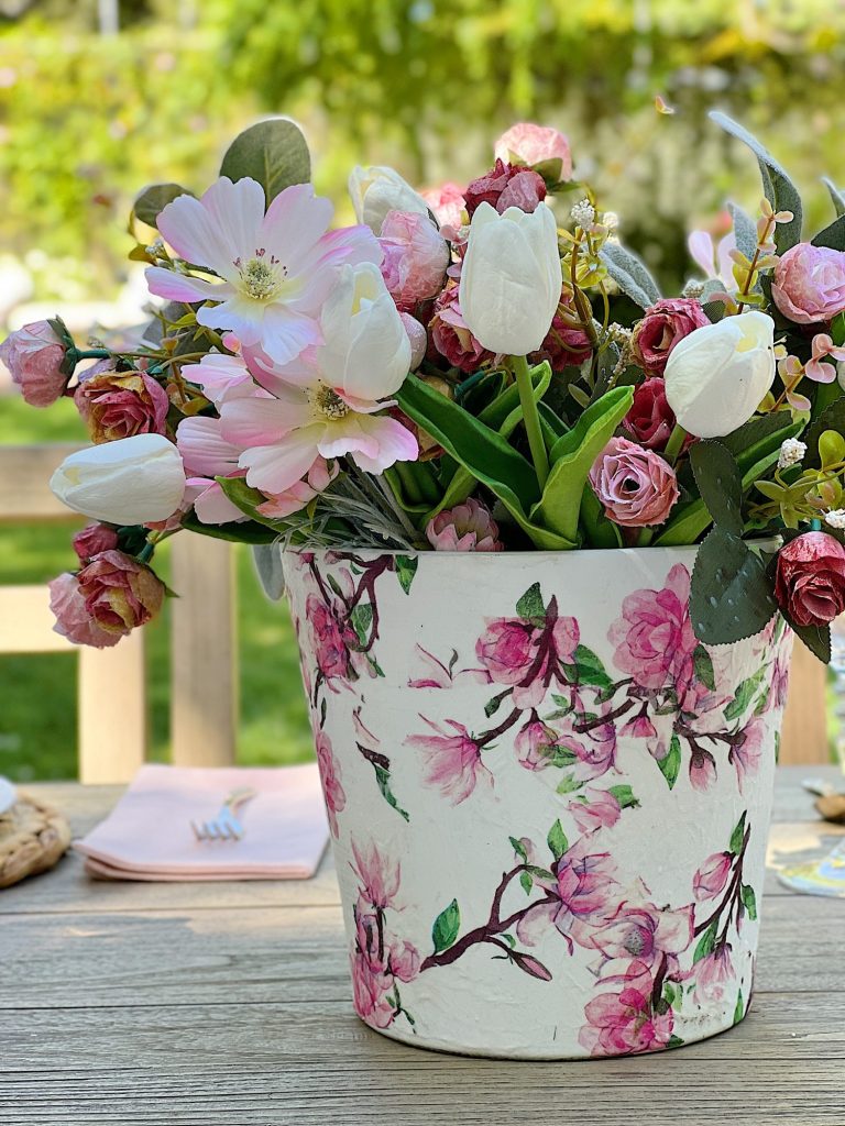A terracotta pot covered with a flowered napkin with faux pink and white flowers.
