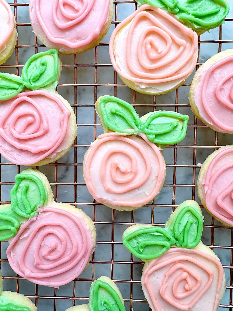 Flower shaped cookies decorated with bright colored buttercream frosting.
