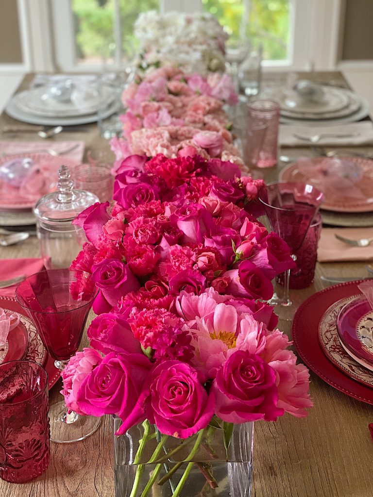 An ombre table with pink flowers down the entire table with table settings also in a pink ombre effect.