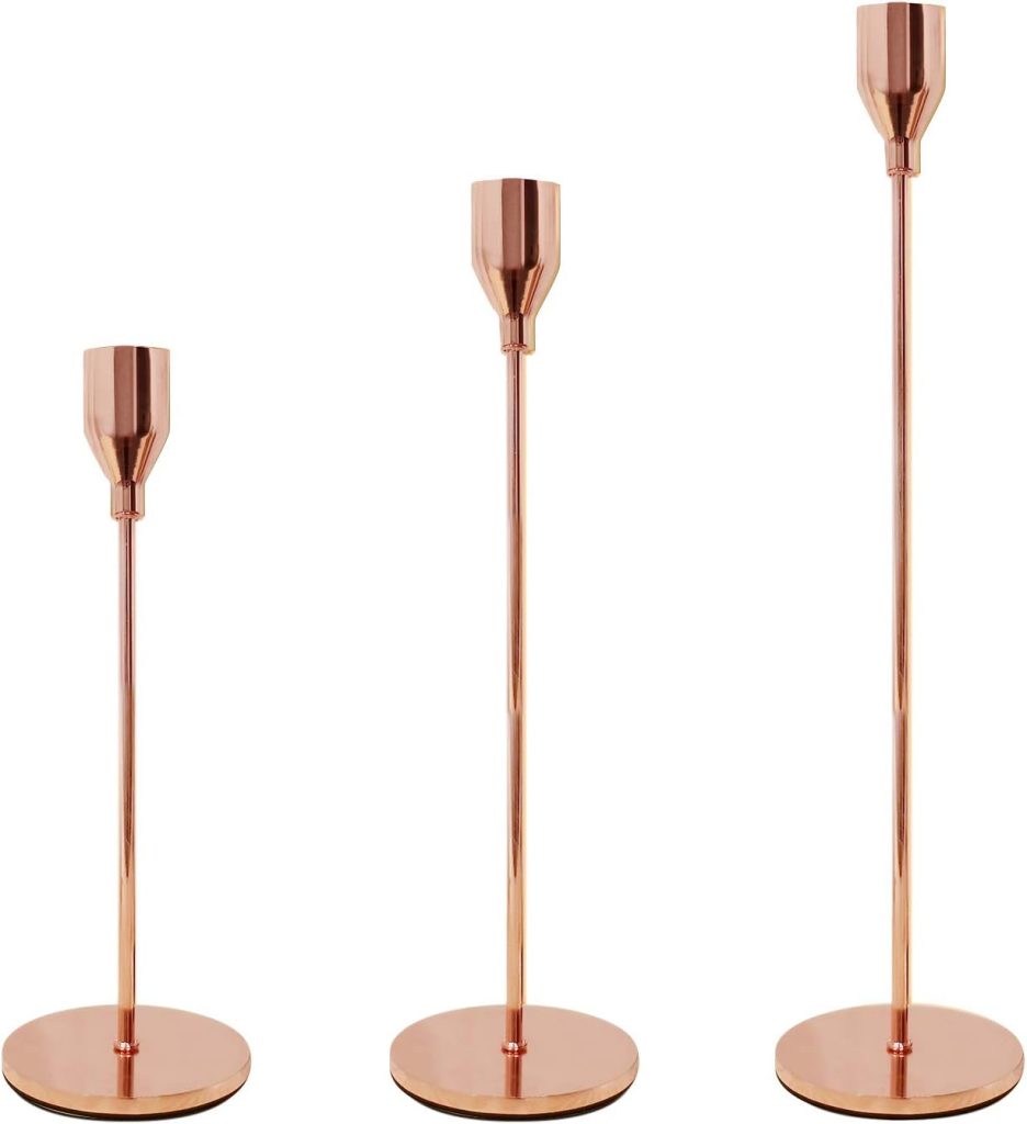 Three copper-colored candlesticks at varying heights with a minimalist design, perfect for an outdoor party ambiance.
