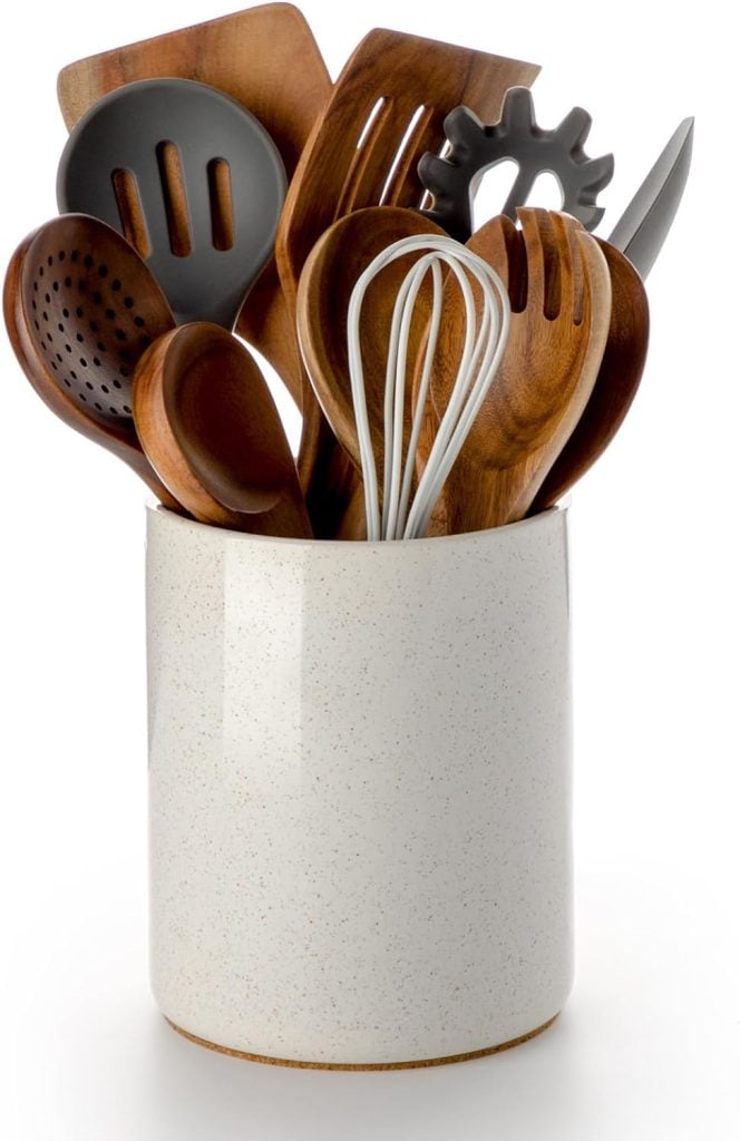 A variety of kitchen utensils stored in a cylindrical container with spring floral arrangements.