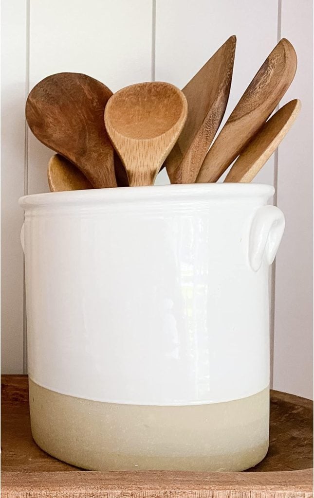 A collection of wooden utensils in a white ceramic crock, adorned with spring floral arrangements.