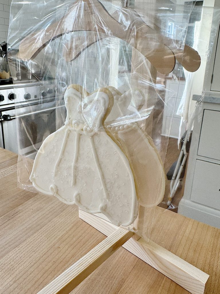 Wedding dress-shaped cookie wrapped in clear cellophane, displayed on a wooden table.